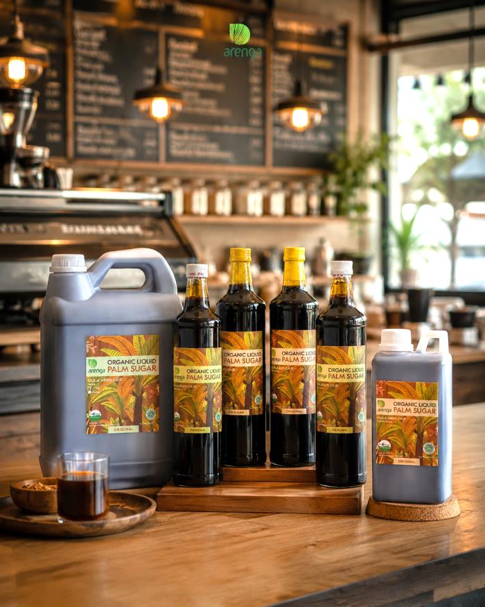Kopi susu gula aren dengan produk gula aren cair Arenga di latar coffee shop, menggambarkan perpaduan kopi dan pemanis untuk menciptakan keseimbangan rasa.