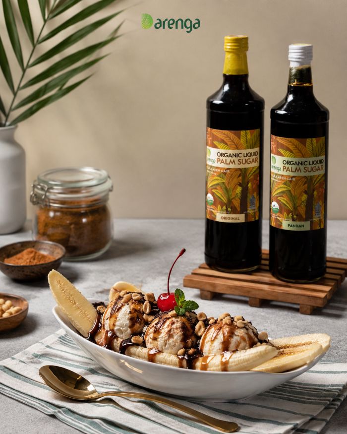Resep banana split gula aren dengan bahan pisang, es krim, saus cokelat, susu, kacang, dan gula aren cair Arenga di atas meja dapur.