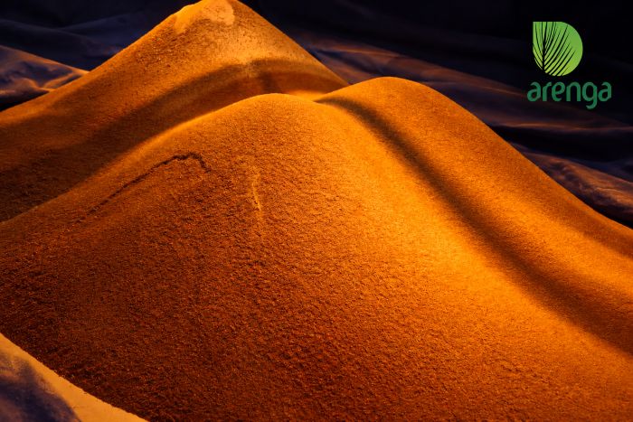 Gula semut aren Arenga berupa hamparan butiran halus berwarna cokelat keemasan dengan tekstur granular, membentuk gundukan di atas latar kain gelap dengan pencahayaan hangat.